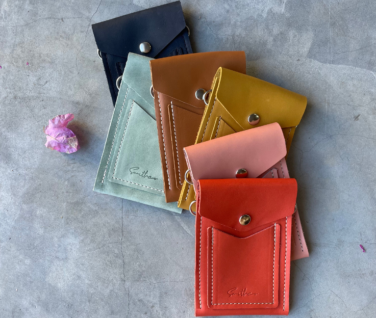 A collection of essential min leather bags in assorted colours set against a concrete screed floor and a pink flower.