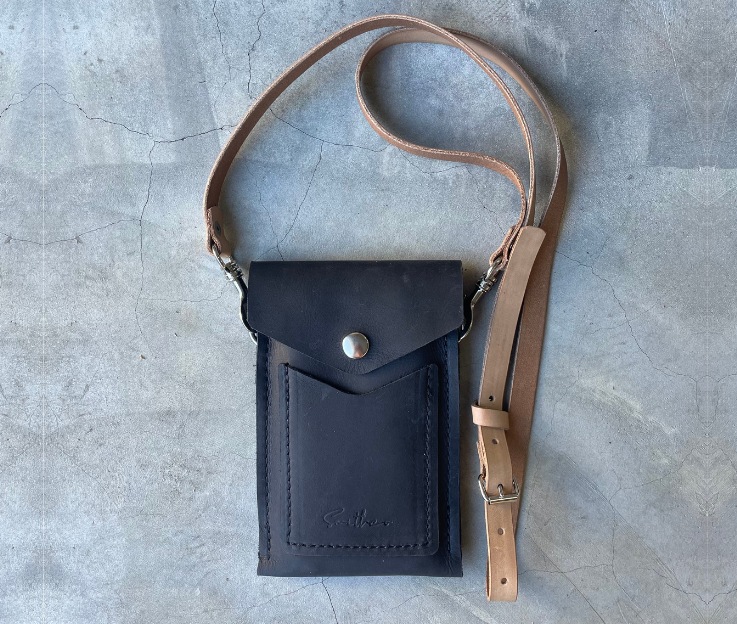 The Smithco Essential mini leather bag in black with a detachable and adjustable leather strap set against a concrete screed floor.