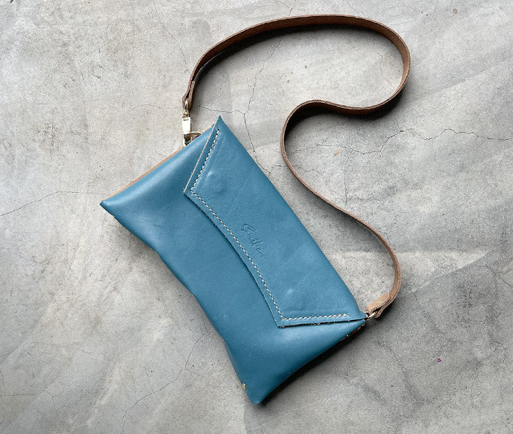 A capri blue leather clutch sized bag with nude coloured detail, stunning curved lines, and studs along the base.