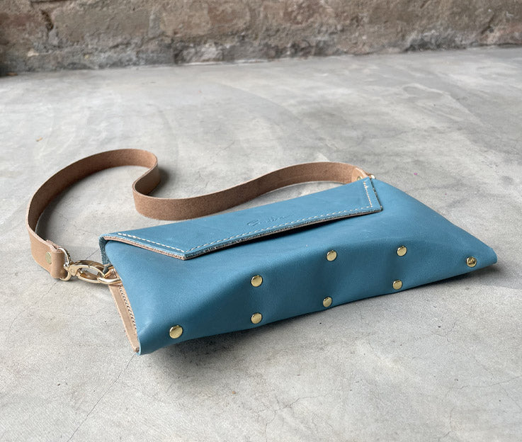 Tje capri blue clutch showing the unique curved and brass studded base