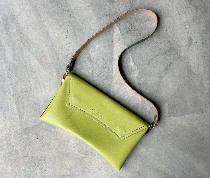 A lime green leather clutch sized bag with hunter green detail, stunning curved lines, and studs along the base.