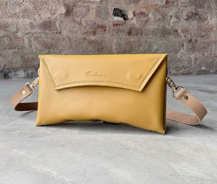 An ochre yellow leather clutch sized bag with nude coloured detail, stunning curved lines, and studs along the base.