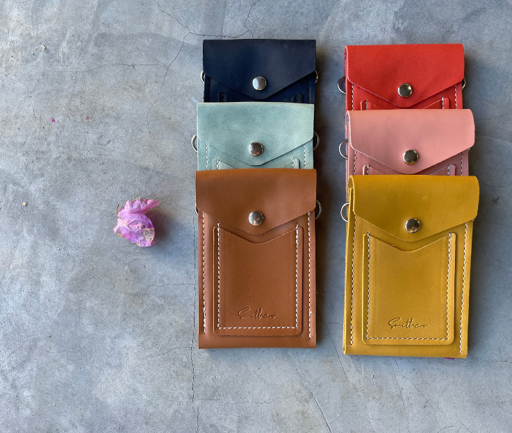 A collection of essential min leather bags in assorted colours set against a concrete screed floor and a pink flower.