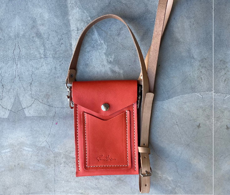 The Smithco Essential mini leather bag in coral with a detachable and adjustable leather strap set against a concrete screed floor.