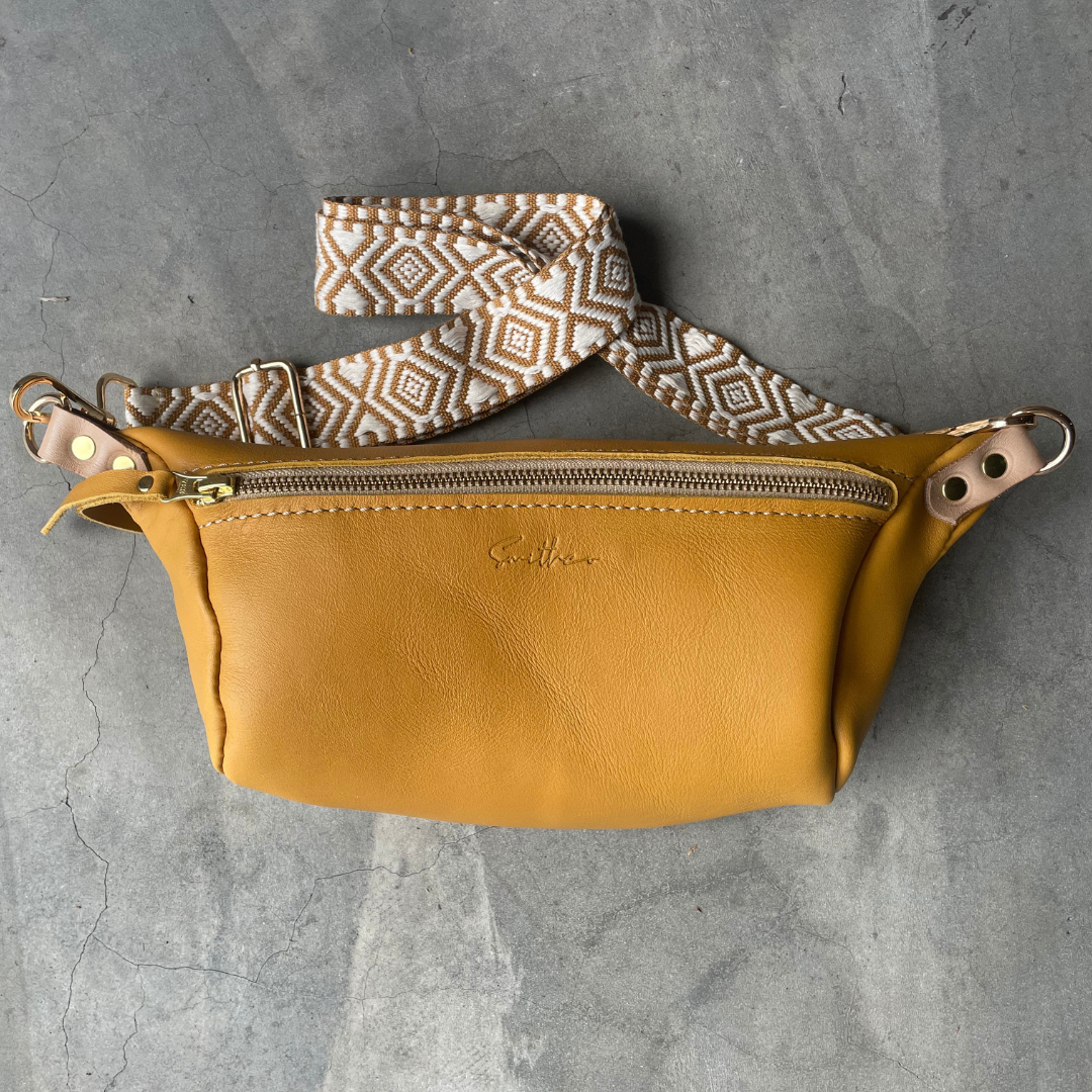 The ochre coloured moon sling bag featured on a concrete screed surface.