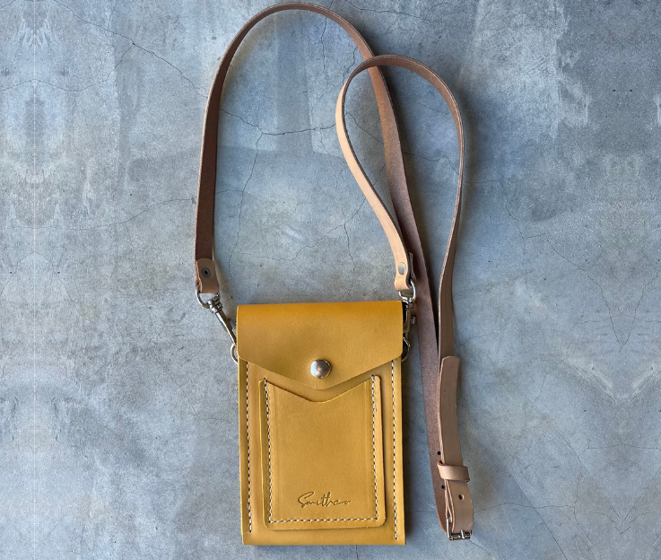 The Smithco Essential mini leather bag in ochre with a detachable and adjustable leather strap set against a concrete screed floor.