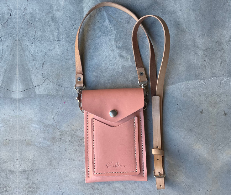 The Smithco Essential mini leather bag in rose with a detachable and adjustable leather strap set against a concrete screed floor.