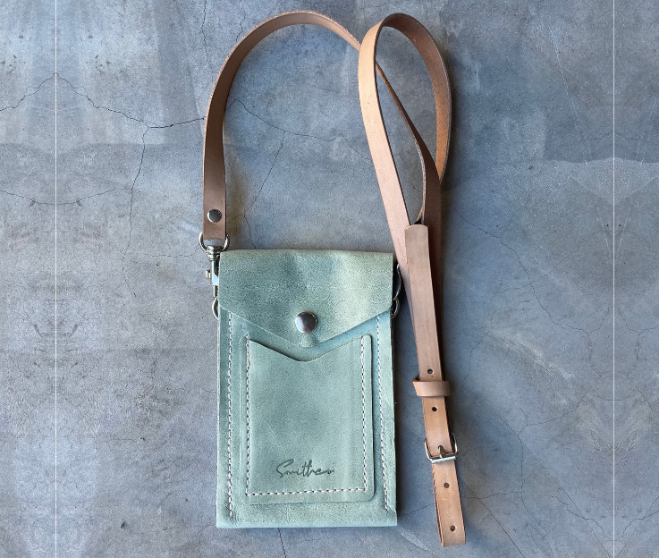 The Smithco Essential mini leather bag in sage green with a detachable and adjustable leather strap set against a concrete screed floor.