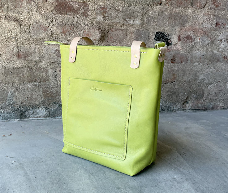 Sassy Shopper steals the spotlight against a sleek concrete screen wall, framed by a backdrop of rustic red brick. The vibrant leather bag in Lime pops with personality, adding a bold touch to the urban-chic scene. #SmithcoSassy #UrbanStyle"