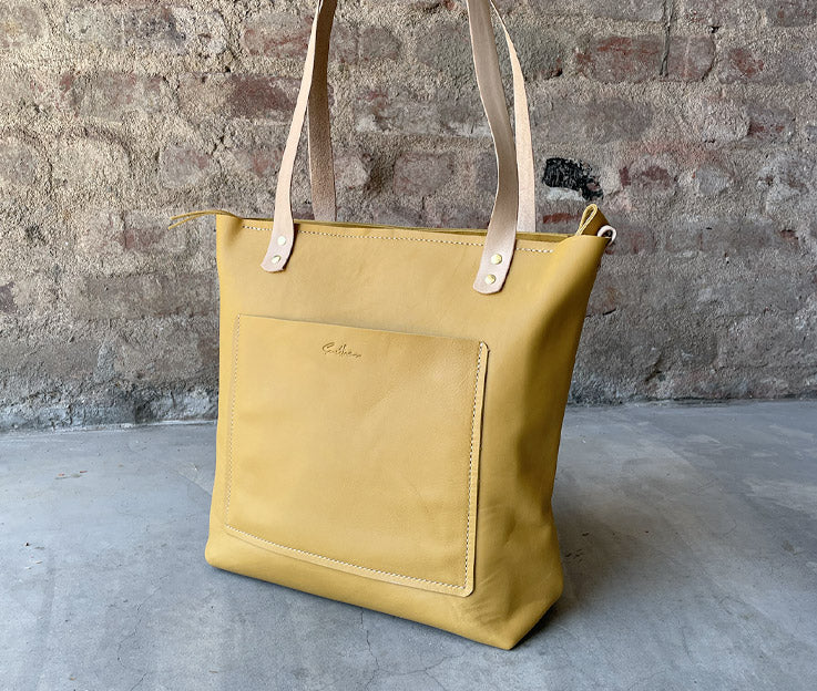 Sassy Shopper steals the spotlight against a sleek concrete screen wall, framed by a backdrop of rustic red brick. The vibrant leather bag in Ochre pops with personality, adding a bold touch to the urban-chic scene. #SmithcoSassy #UrbanStyle"