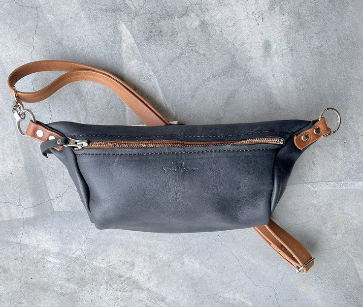 The black and amber moon sling bag featured on a concrete screed surface.