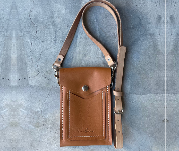 The Smithco Essential mini leather bag in tan with a detachable and adjustable leather strap set against a concrete screed floor.