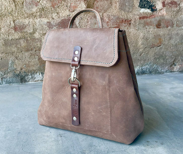 Brown leather backpack with brown detail. Boasts secure pocket, key clip, inner pocket and power bank cable porthole. Closes securely with a metal clip.