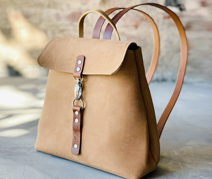 Fudge coloured leather backpack with amber detail. Boasts secure pocket, key clip, inner pockets and power bank cable porthole. Closes securely with a metal clip.