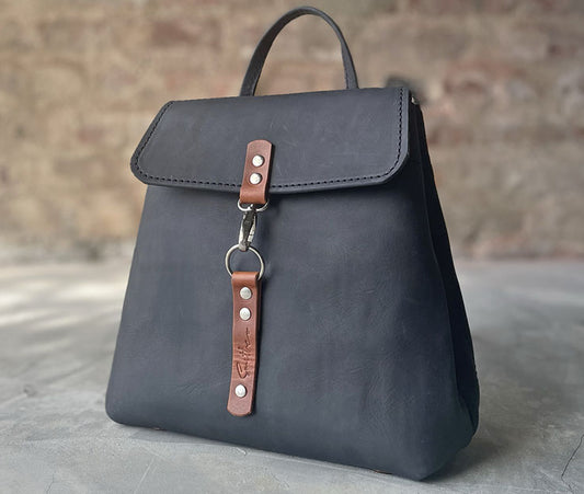 Black leather backpack with amber detail. Boasts secure pocket, key clip, inner pockets and power bank cable porthole. Closes securely with a metal clip.