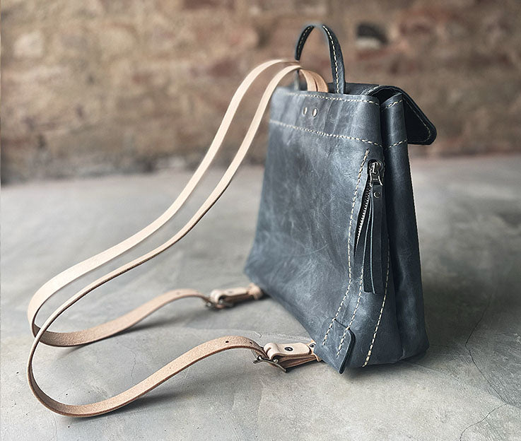 Side view of the Denim blue leather backpack with the secure easy access pocket and adjustable shoulder straps in a nude colour. 